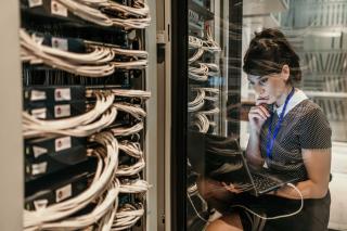 Woman working on laptop with racks of servers in a server room.