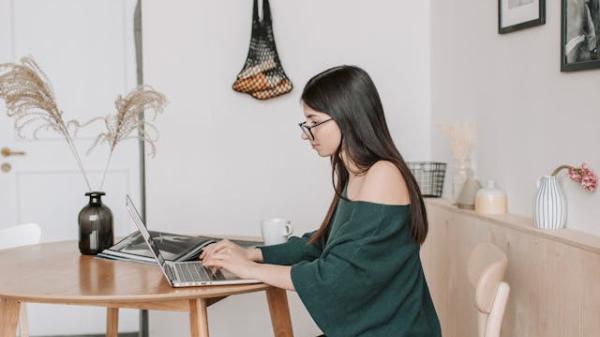 woman sat at dining table at home working on a laptop