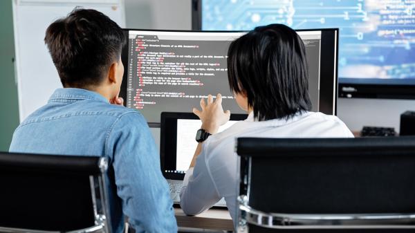 Two developers reviewing code together on a large monitor
