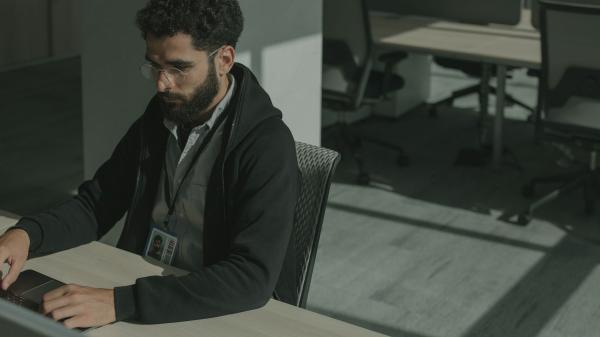 Security engineer with an ID badge working at a laptop in an office