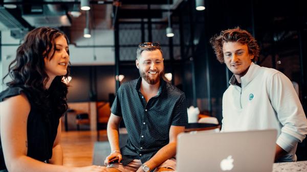 Three colleagues reviewing work together on a laptop