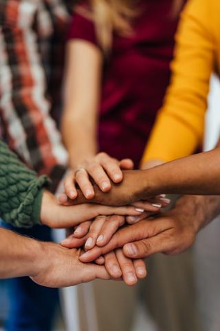 Group of people placing hands together, one on top of the other.