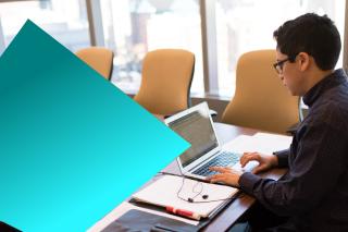 Male IT professional working at a meeting room office desk using a laptop.