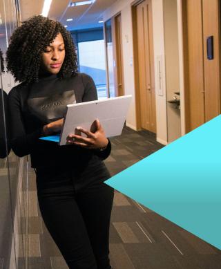 Female IT professional working on her laptop while standing next to a server room.