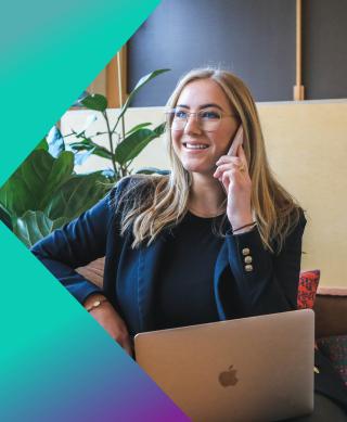 Female IT speaking on smart phone while working on her laptop.