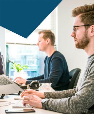 Two male IT professionals sat at their desks while working on desktops.