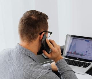 Professional male working at a laptop while using a smart phone.