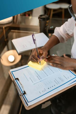 Woman writing on a post-it note with a printed CV in front of her