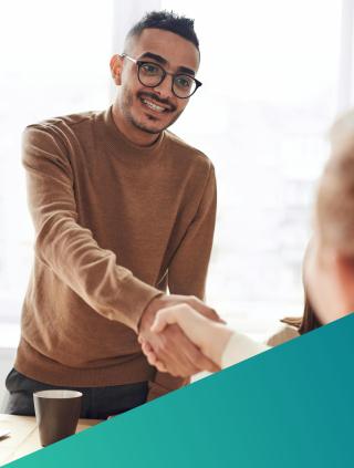 A professional male recruiter in a brown sweater smiling warmly while shaking hands with a candidate or client, visually representing a successful hiring outcome and the strategic recruitment partnership required for the 2026 Cloud and DevOps market.