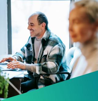 A cheerful software engineering manager in a plaid shirt reviewing market intelligence data on a laptop, illustrating Deerfoot’s data-driven approach to Software Engineering and QA recruitment.