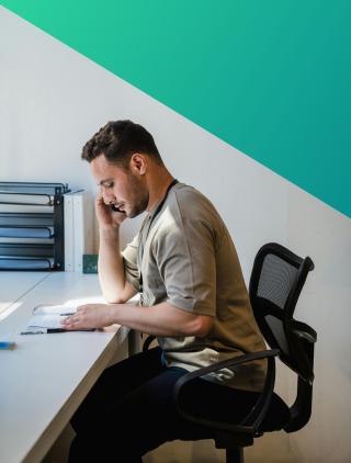 Employee sat at a desk writing onto notepad whilst on the phone