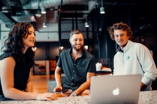 Three colleagues reviewing work together on a laptop