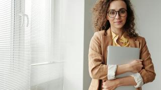 Female professional looking straight to camera holding a laptop.