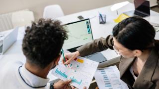 Two data professionals looking at paper documents and working on a laptop.