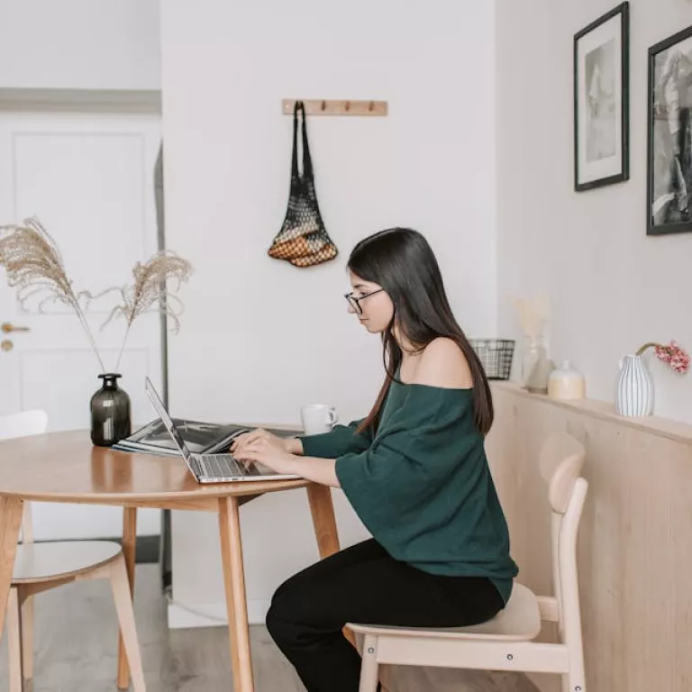 woman sat at dining table at home working on a laptop